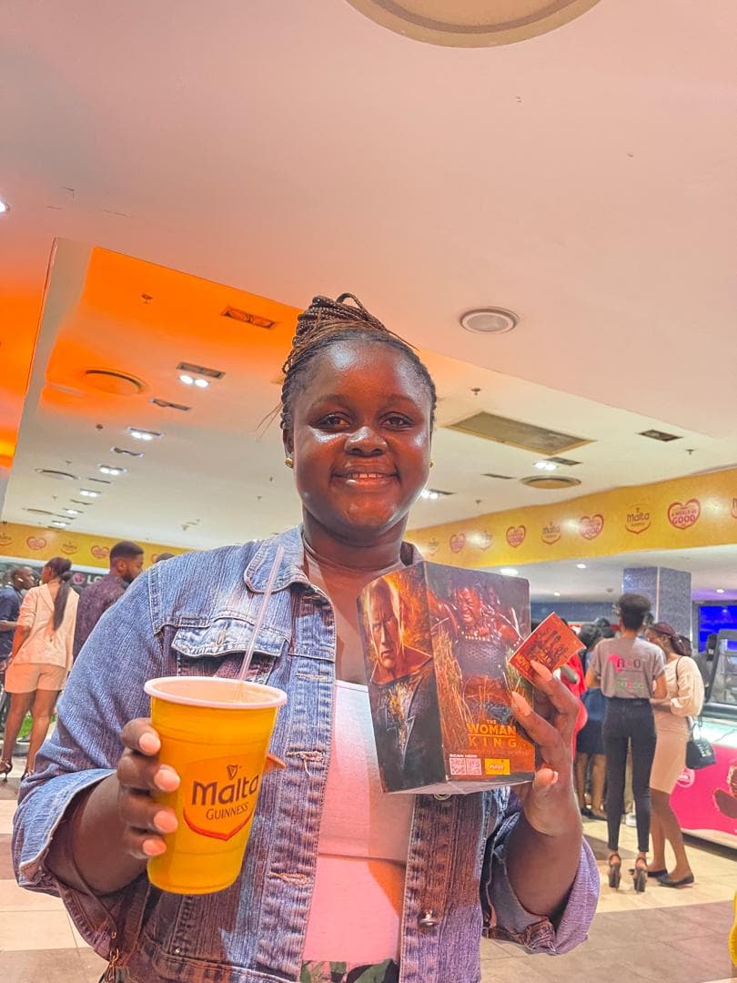 A guest at a cinema activation holding a Malta Guinness cup and a The Woman King box